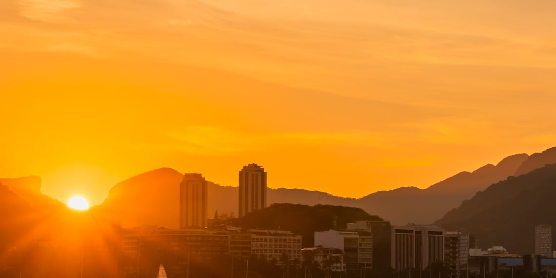 Imagem panorâmica do Rio de Janeiro com sol em destaque.